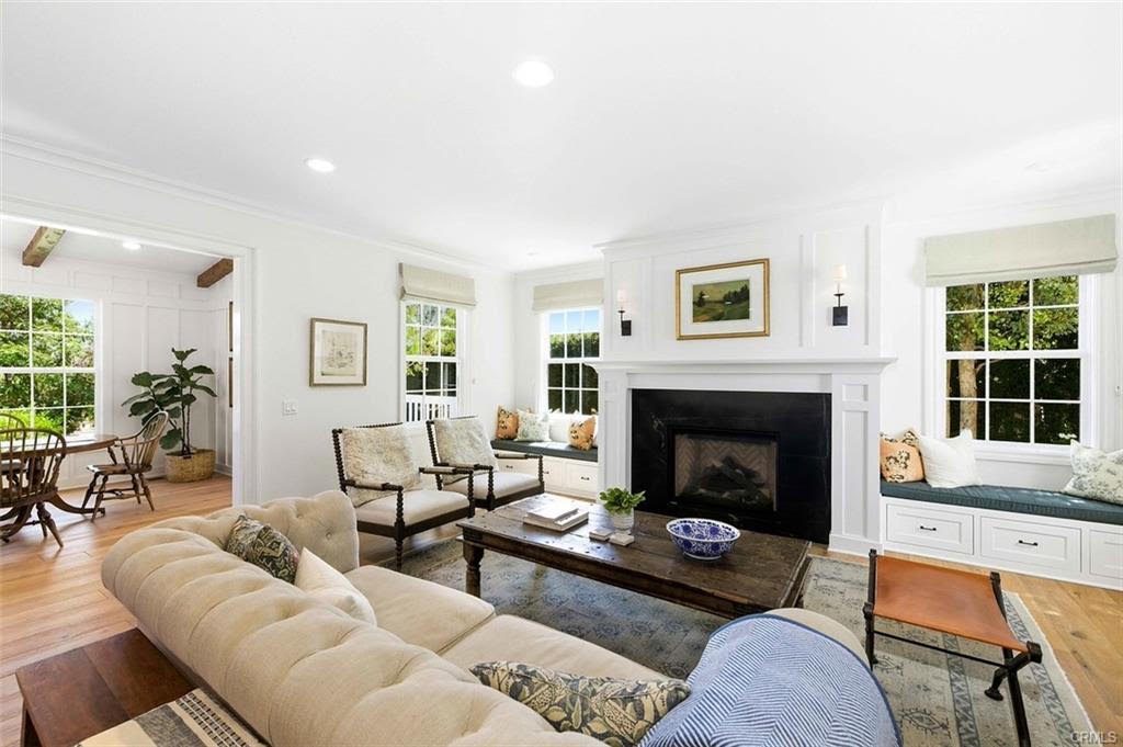 Living room with a tufted cream sofa, a white fireplace with built-in window seats and hardwood floors