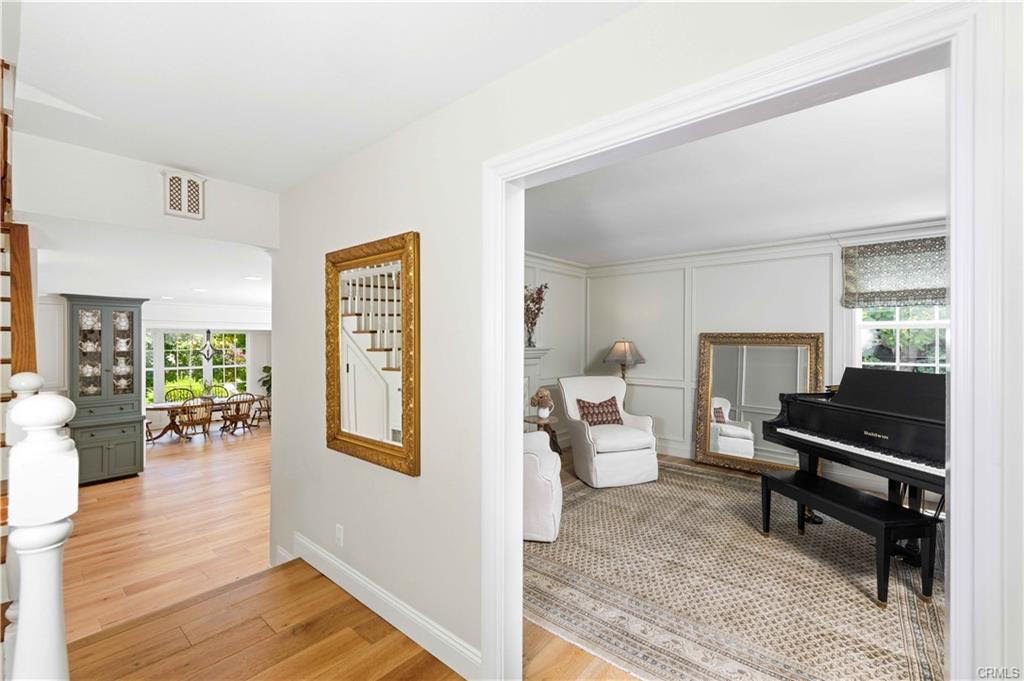 Entry hallway with a gold framed mirror, opening to a sitting room with a black grand piano and a dining area beyond
