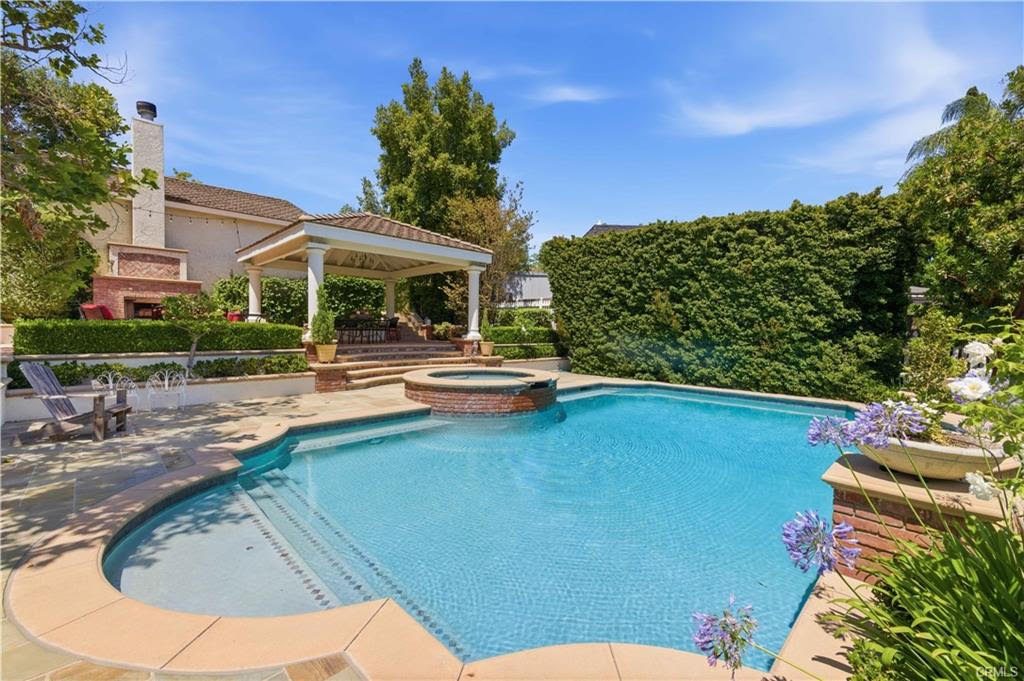 Backyard pool and spa with a covered pavilion and an outdoor brick fireplace behind them