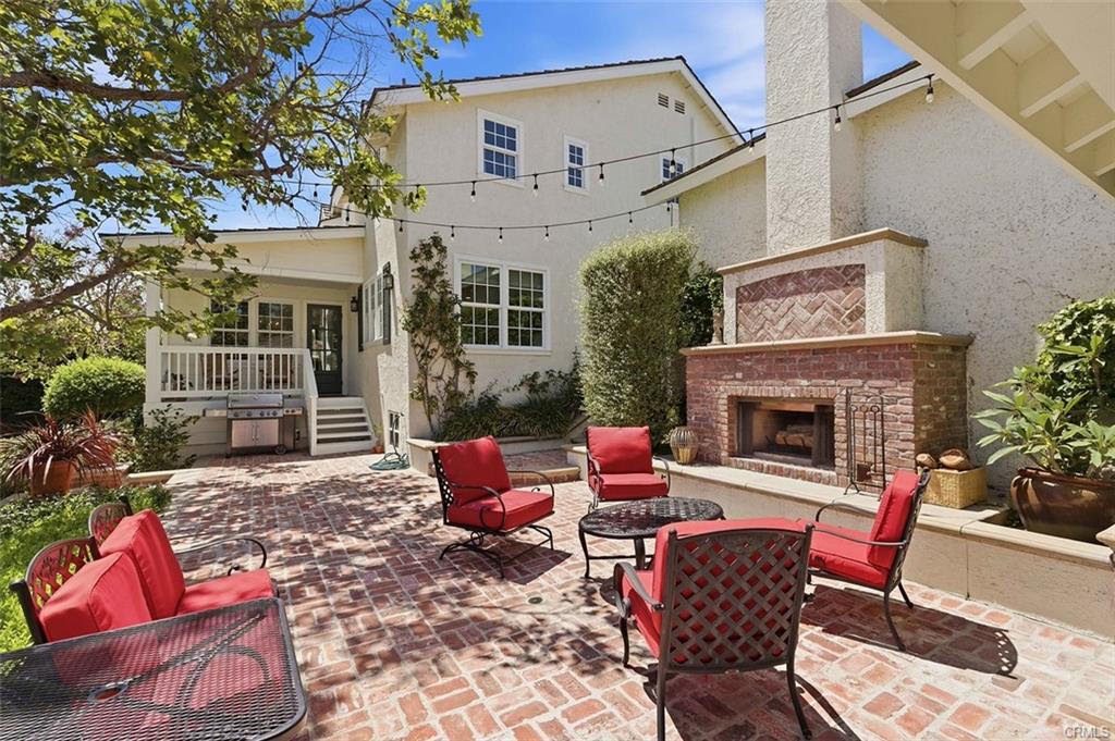 Brick patio with red cushioned chairs around an outdoor brick fireplace, with string lights overhead