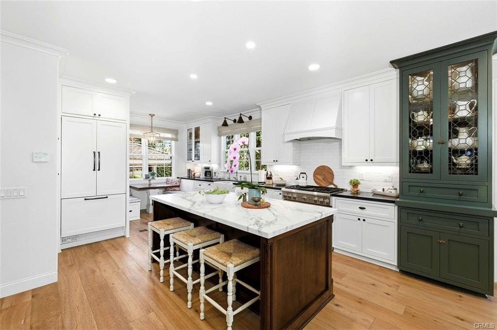 Kitchen with a marble island, three woven bar stools, white cabinets and a green glass-front china cabinet